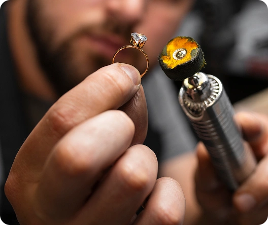 Close-up van een juwelier die een diamanten verlovingsring polijst met professionele tools, waarbij vakmanschap, precisie en luxe juwelencreatie worden benadrukt.