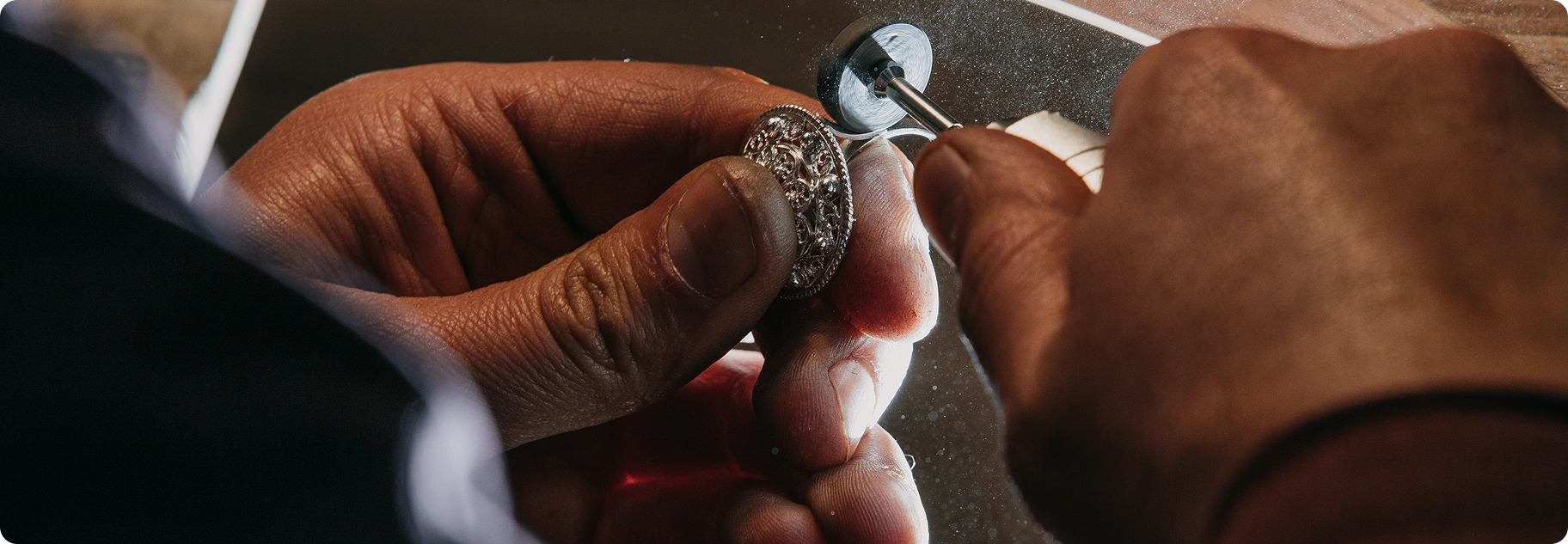 Close-up van een juwelier die een ingewikkelde metalen ring polijst met professionele apparatuur, waarbij precisievakmanschap en fijne juwelenproductie worden benadrukt.