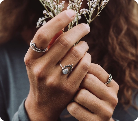Artistieke close-up van handen die meerdere bohemian-stijl ringen dragen terwijl ze delicate witte bloemen vasthouden in natuurlijk warm licht.